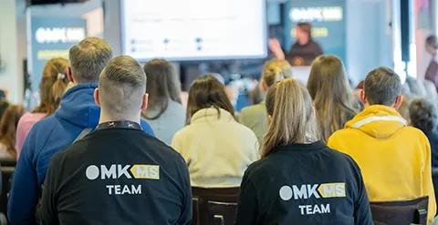 OMKMS Team Kolleg:innen mit Vortrag im Hintergrund